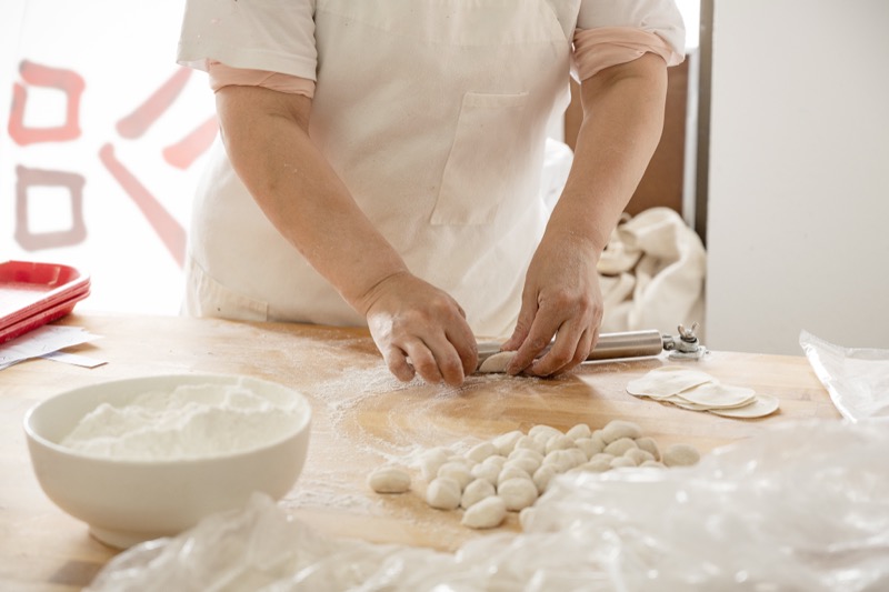 Hands rolling dumpling wrappers from scratch